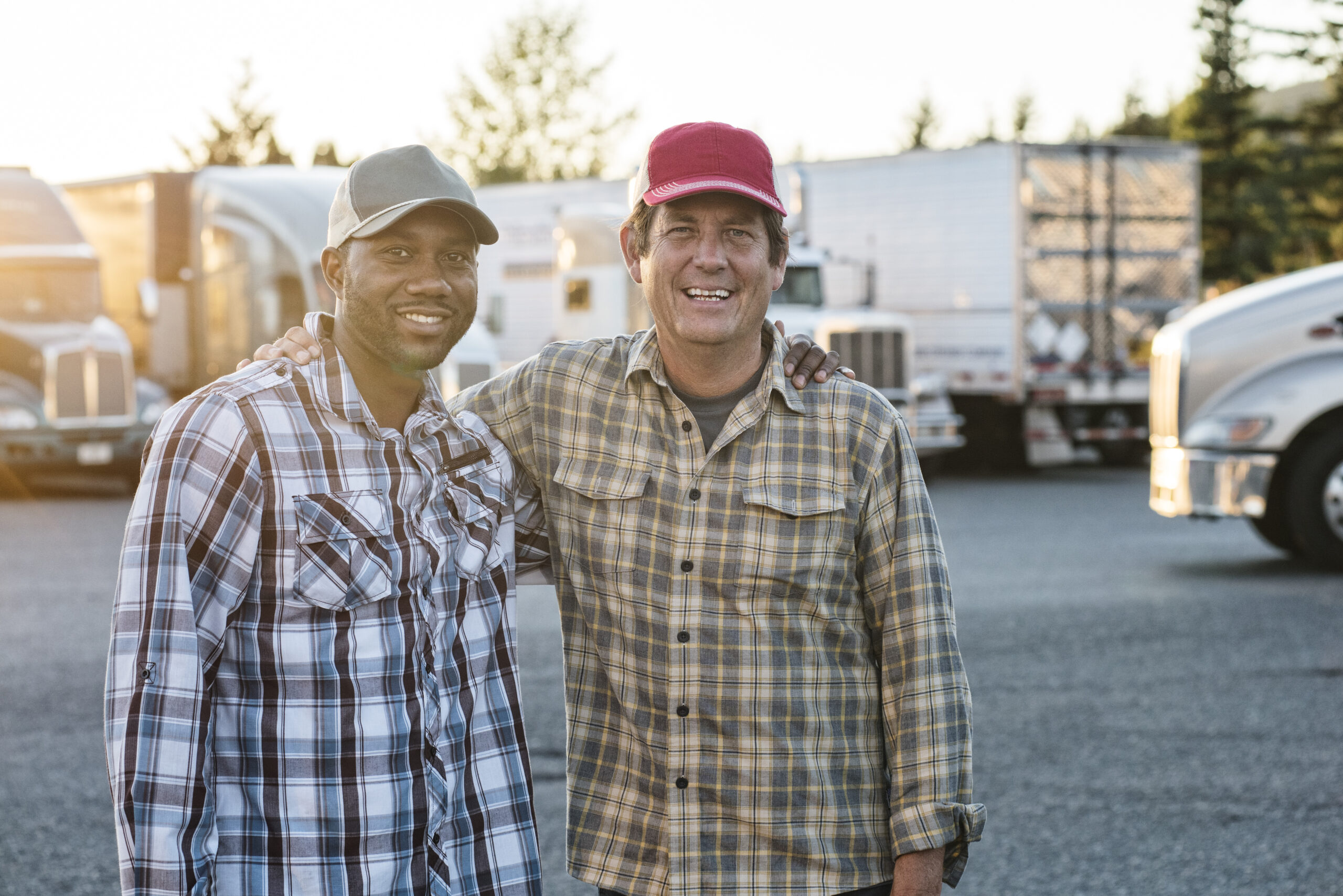 A caucasian man and a black man truck driving team together in a truck stop parking lot.